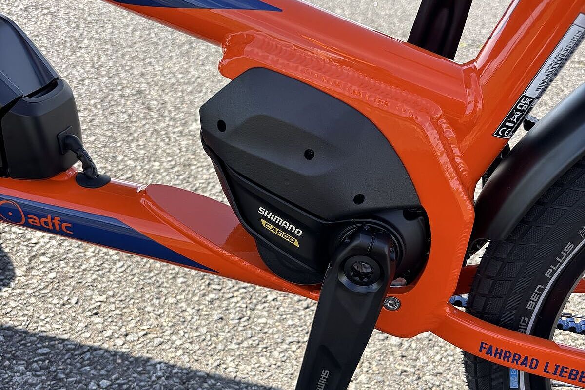 Chike Antrieb Der Motorbereich eines orangefarbenen E‑Lastenrads mit schwarzem Mittelmotor und Kurbelarm.