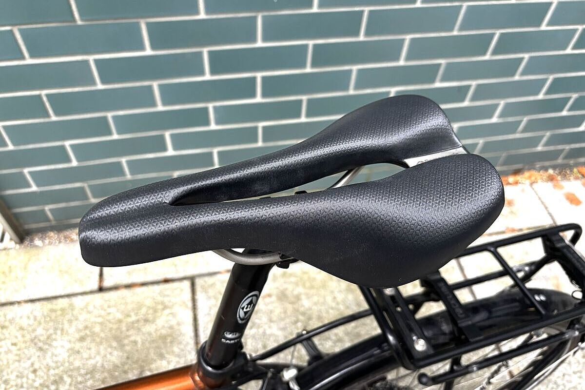 Personomic Schwarzer Fahrradsattel mit langer Öffnung, montiert an einem Fahrrad vor einer grünen Kachelwand.